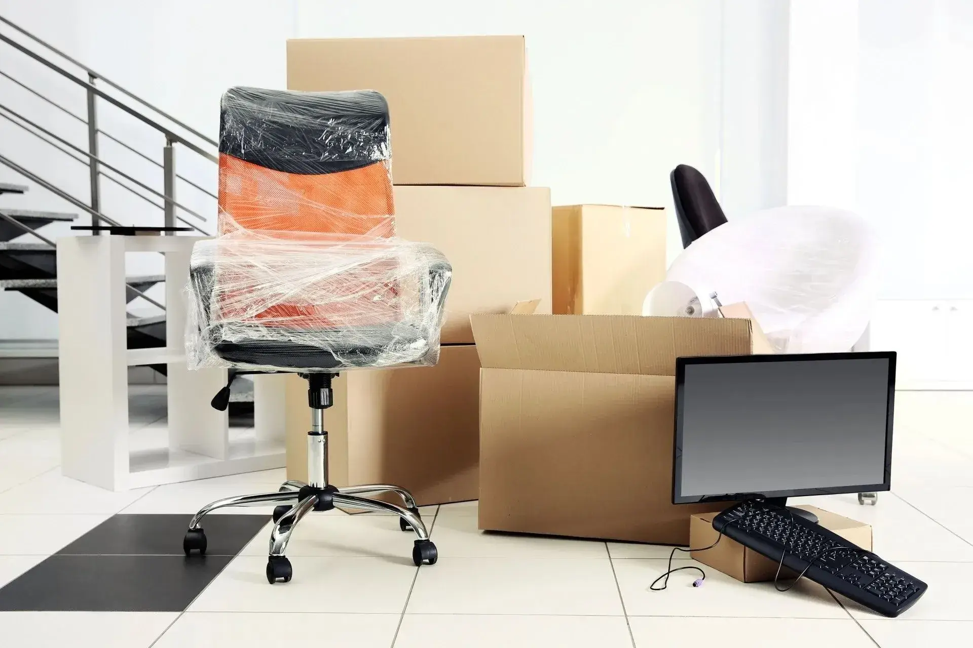 Plastic-wrapped office chair, desktop monitor, and cardboard boxes prepped for a commercial office move.