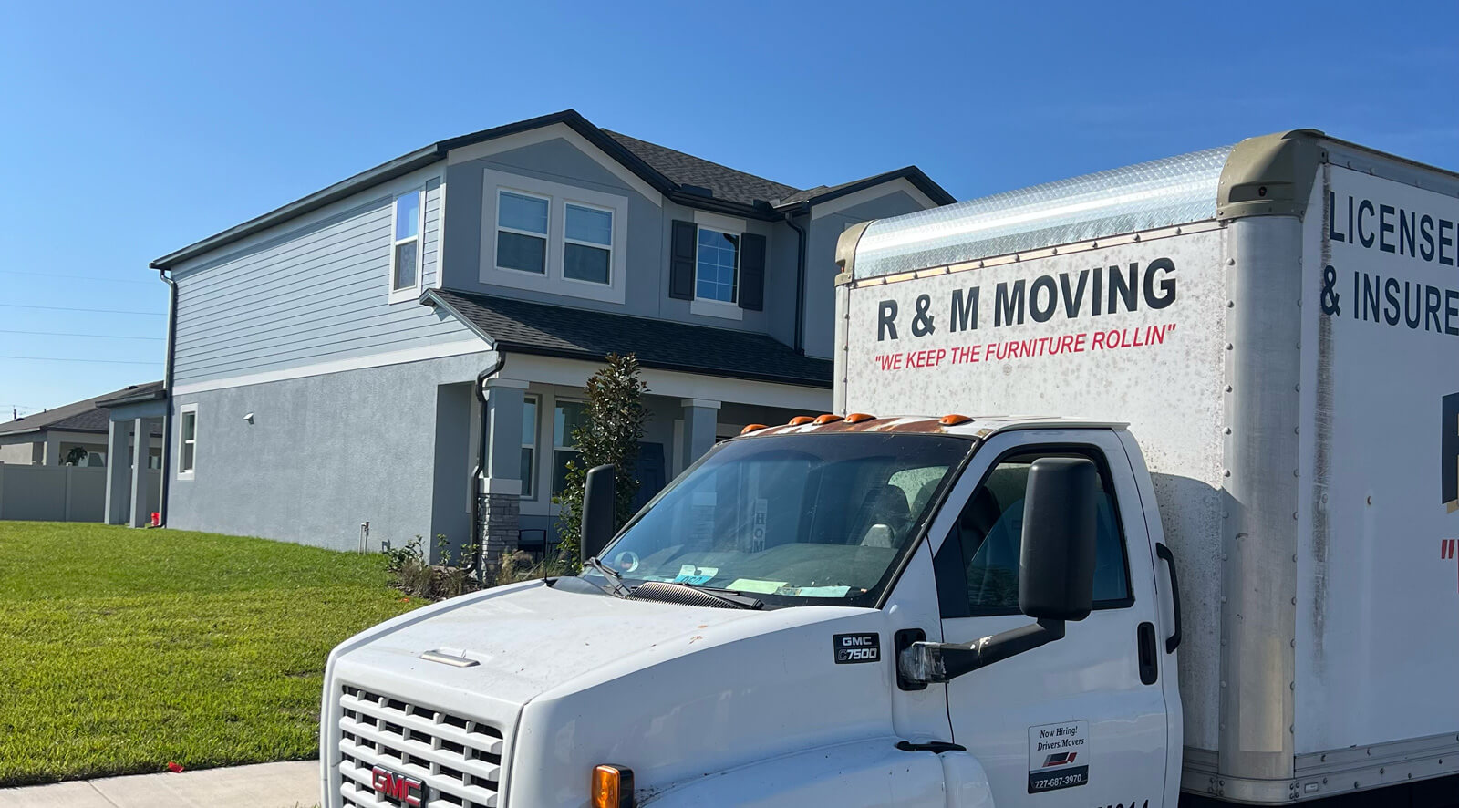 Front view of an R & M Moving truck parked in front of a two-story suburban home on a sunny day.