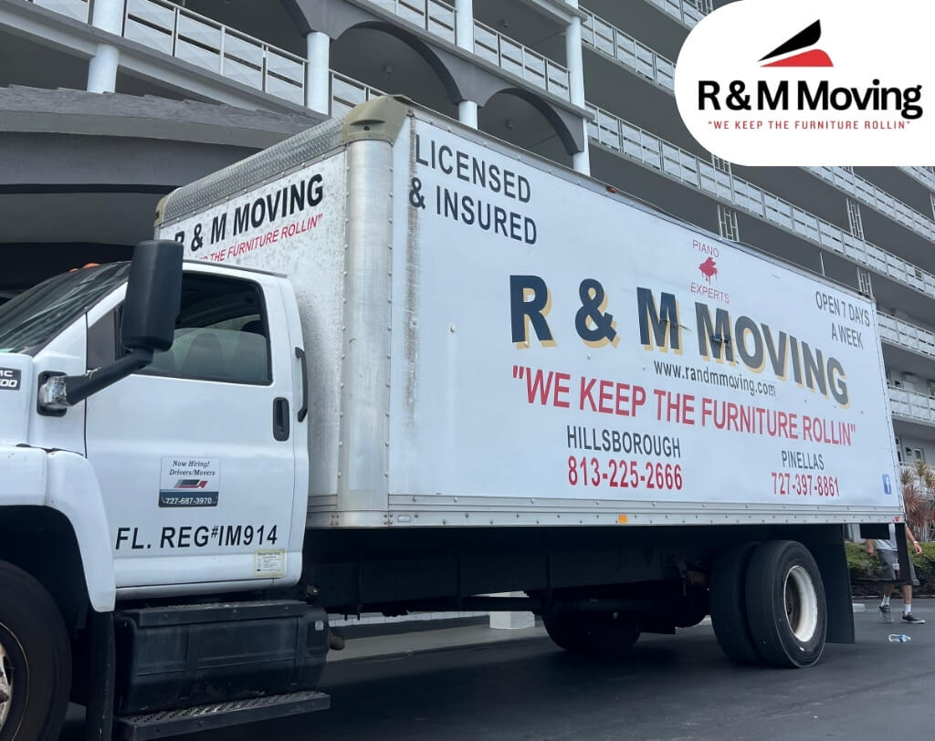 White delivery truck parked on a street, with “R&M Moving” and a phone number on the side, and other vehicles and buildings in the background.