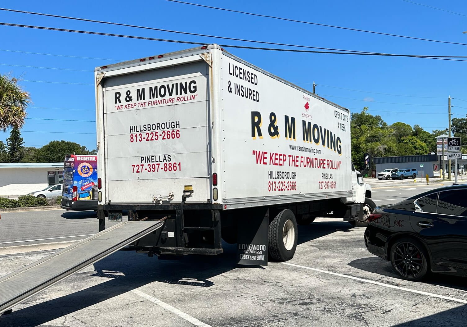 Rear view of an R & M Moving truck with the unloading ramp extended in a parking lot.