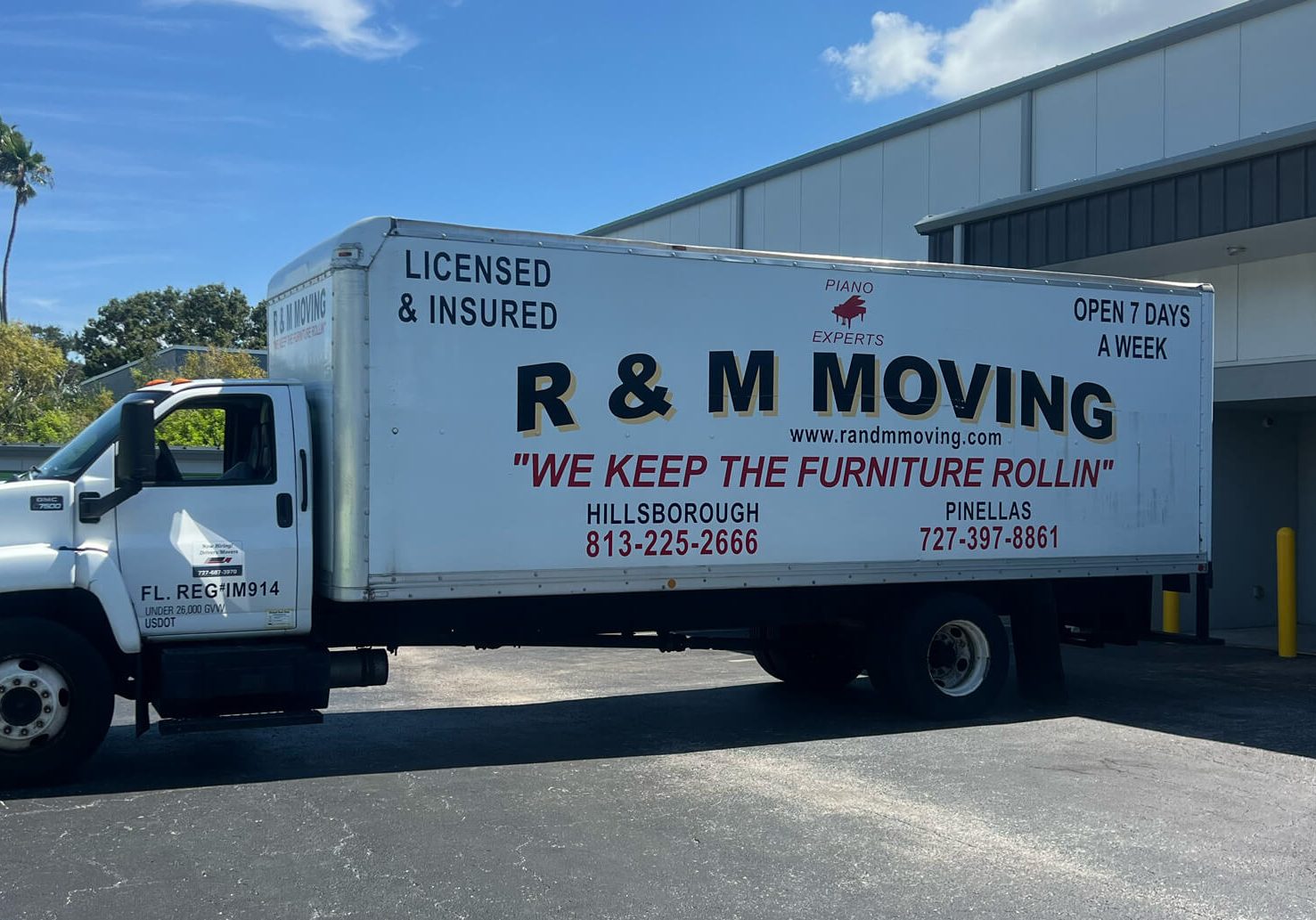 Side profile of an R & M Moving truck parked at a commercial facility highlighting piano moving expertise and licensed insured services.